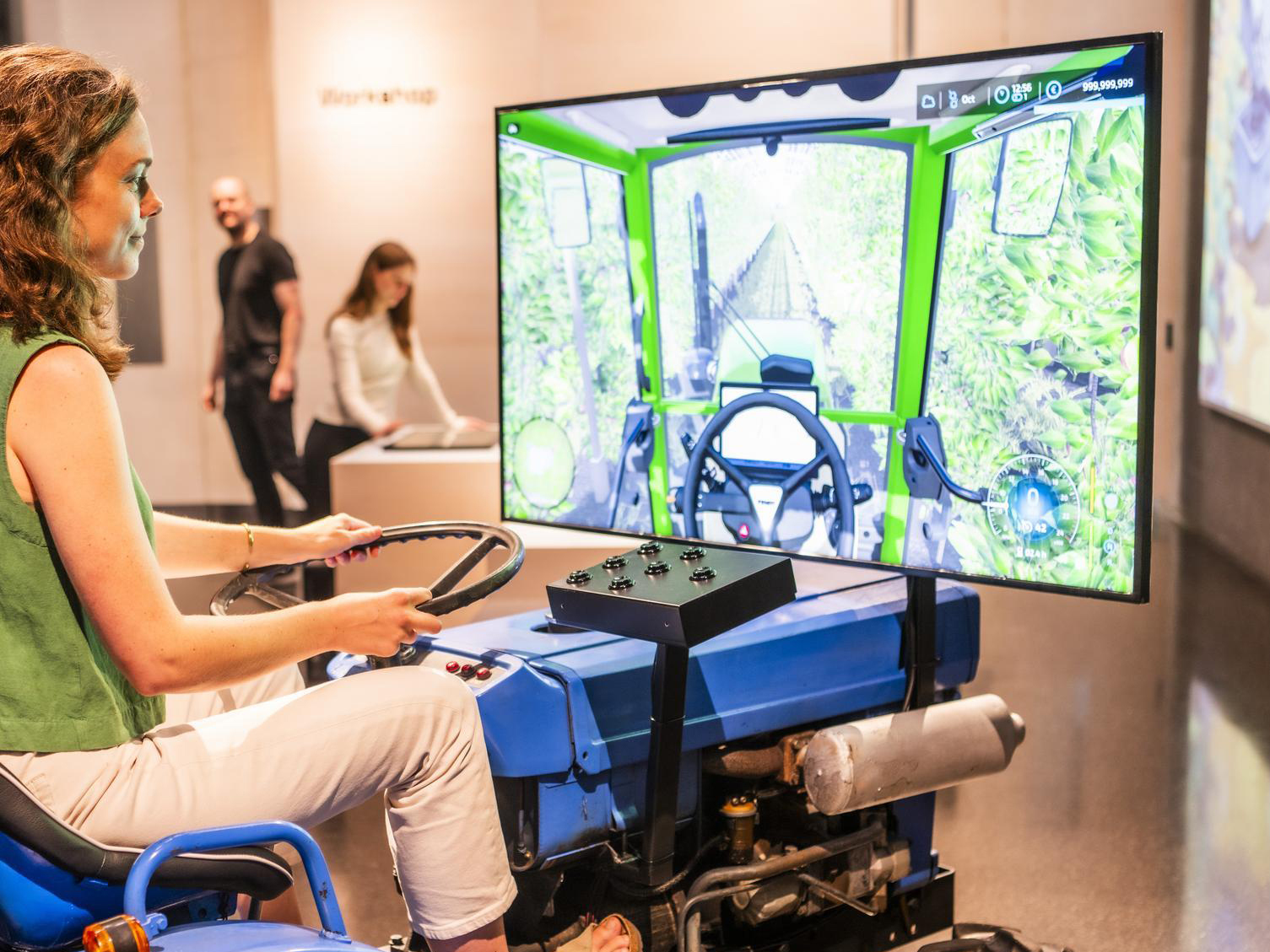 Eine Frau sitzt auf einem kleinen Traktor, vor ihr ein Bildschirm mit der Simulation eines Feldes