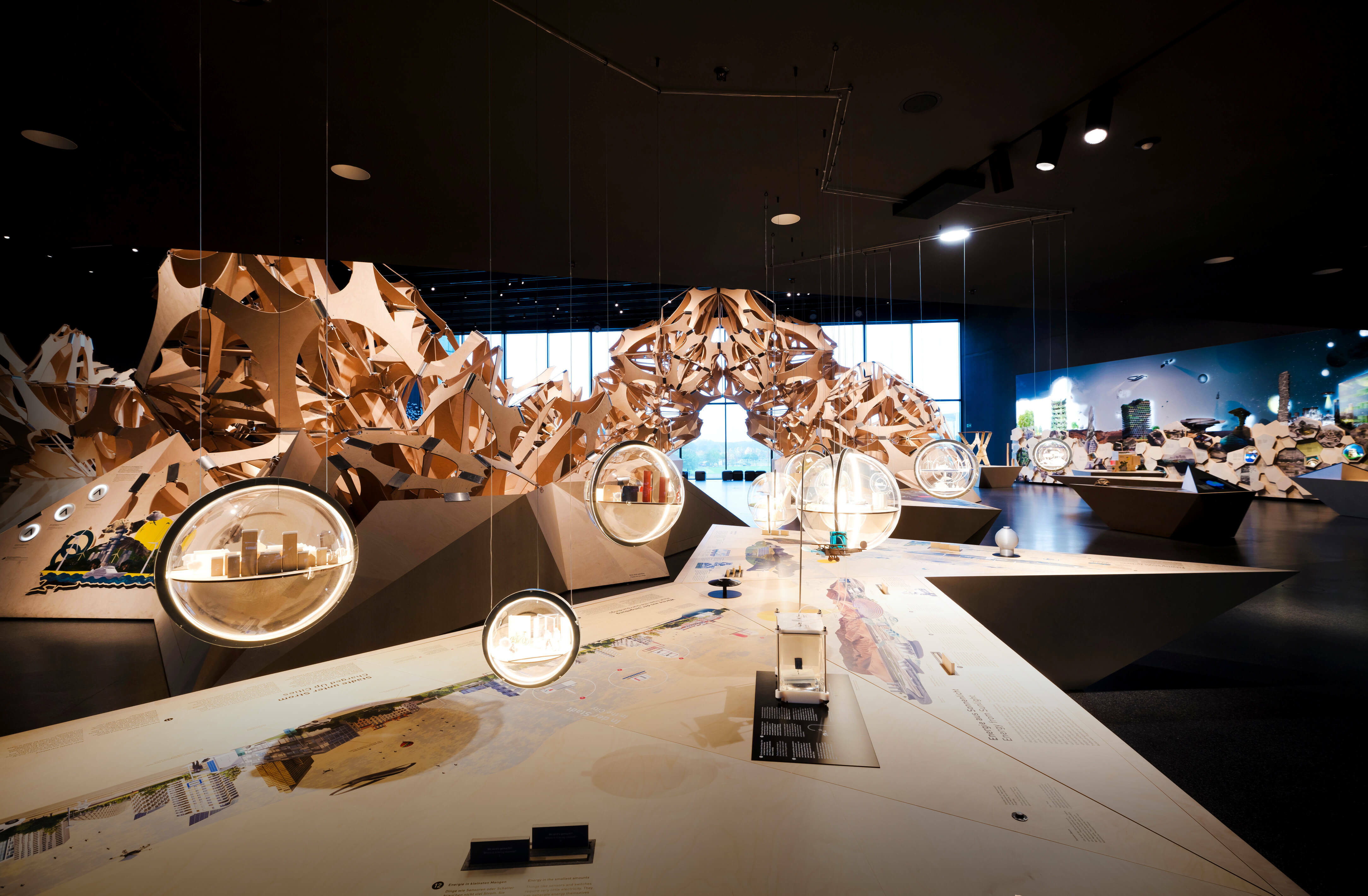 Der Denkraum Natur mit einer großen Holzskulptur im Hintergrund. Im Vordergrund baumeln Glaskugeln mit kleinen Modellen von Städten