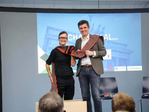 Futurium-Direktor Stefan Brandt übergibt den Riesenschal an Veronika Springmann, Leiterin des Sportmuseums.