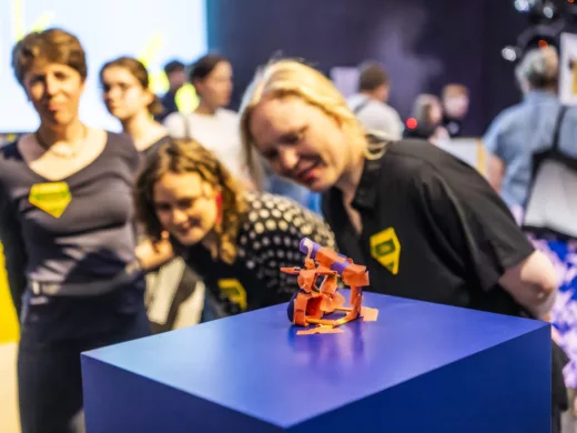 Ein Fahrrad gebastelt aus Pappe steht auf einem Podest. Menschen betrachten es.