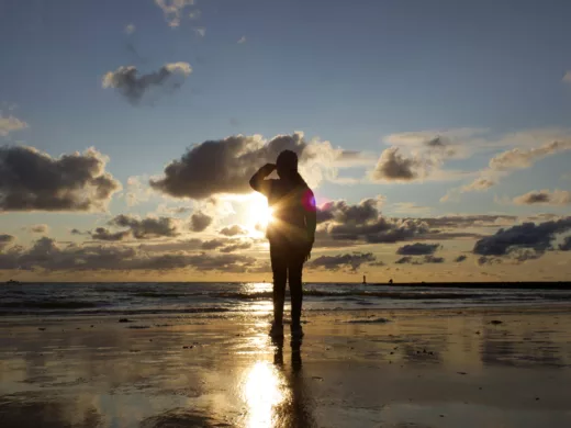 Eine Person steht im Sonnenuntergang am Strand und blickt in die Ferne