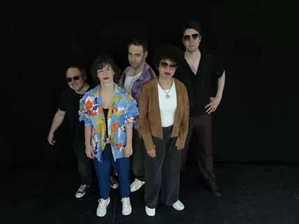 Fünf Personen in bunter Kleidung stehen vor einem schwarzen Hintergrund.