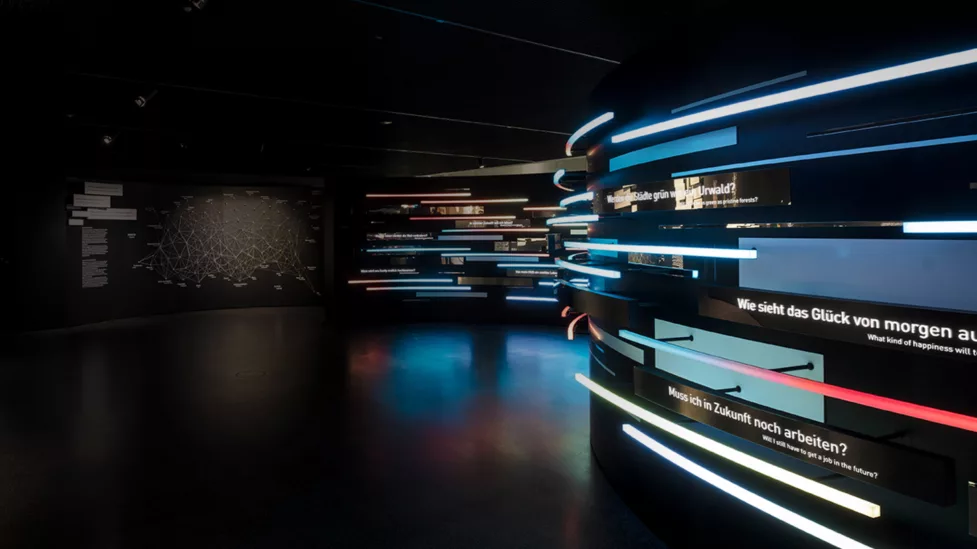 A dark wall is illuminated by colourful strips of light. The question ‘Do I still have to work in the future?’ is written on the wall.