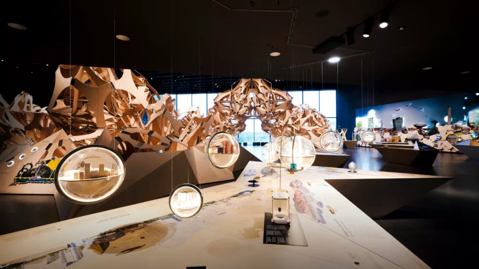The nature thinking space with a large wooden sculpture in the background. Glass spheres with small models of cities dangle in the foreground