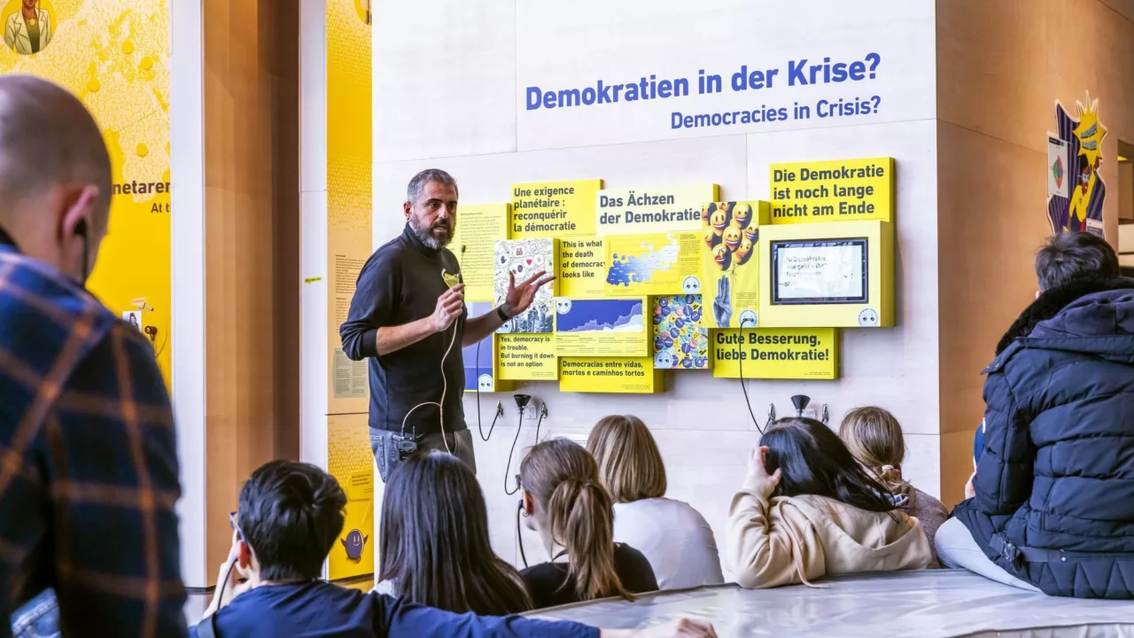 Jugendliche sitzen in der Ausstellung, während ein Guide etwas erklärt