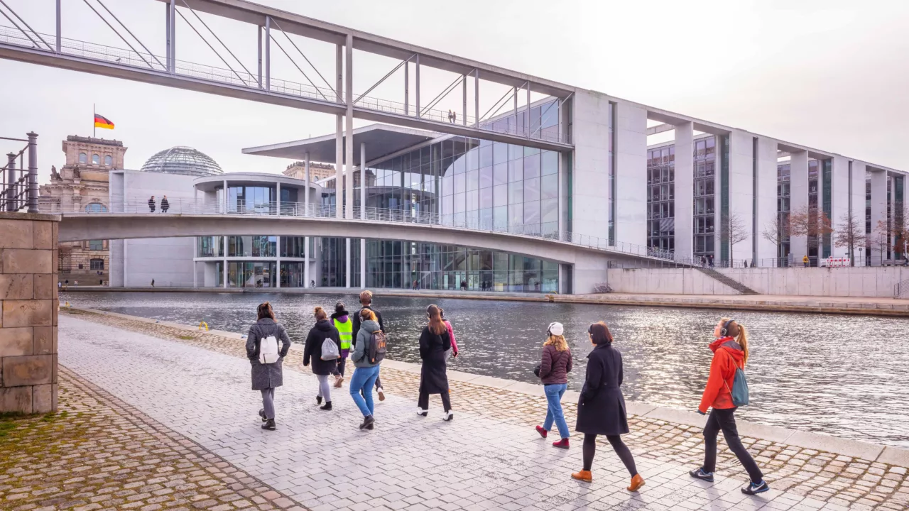 A group of people wearing headphones walk past the Chancellery.