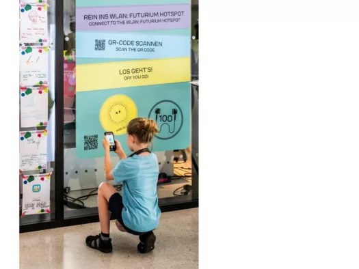 Ein Junge kniet vor einem Plakat und scannt mit dem Smartphone einen QR-Code