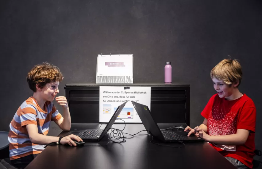 Zwei Kinder sitzen sich mit Computern gegenüber