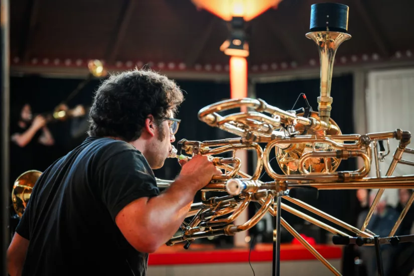 Ein Mann spielt auf einem Blechblasinstrument, das aus mehreren zusammengefügten Instrumenten besteht