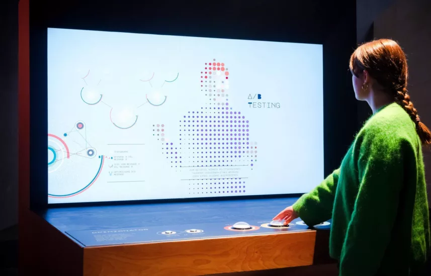 A woman stands in front of a screen and presses a button with her hand.