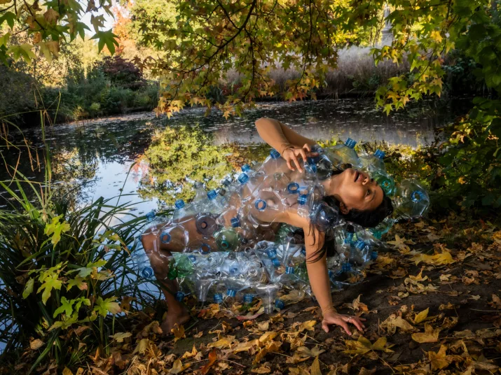 Woman in a costume made from recycled plastic at an autumnal pond.