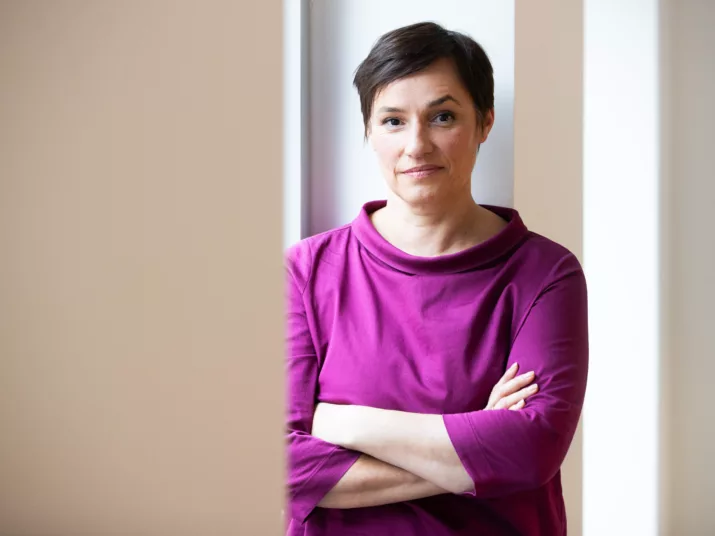 Nicole Deitelhoff seht mit verschränkten Armen vor einem hellen Hintergrund. Sie trägt ein fliederfarbenes Oberteil.