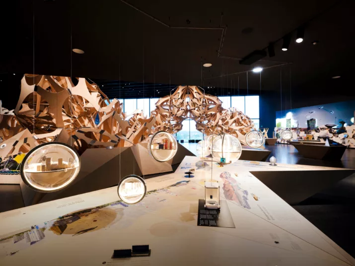 Der Denkraum Natur mit einer großen Holzskulptur im Hintergrund. Im Vordergrund baumeln Glaskugeln mit kleinen Modellen von Städten