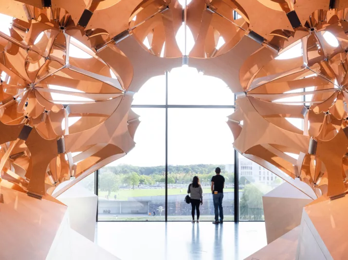 Two people stand under the wooden sculpture “Neo-Nature” in the Futurium exhibition.