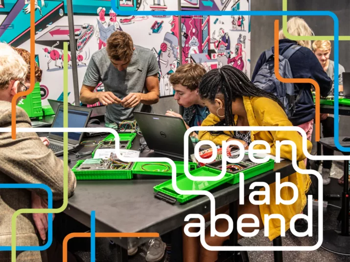 Fünf Menschen verschiedener Altersgruppen sitzen an einem Tisch und experimentieren an technischen Baukästen und Computern.